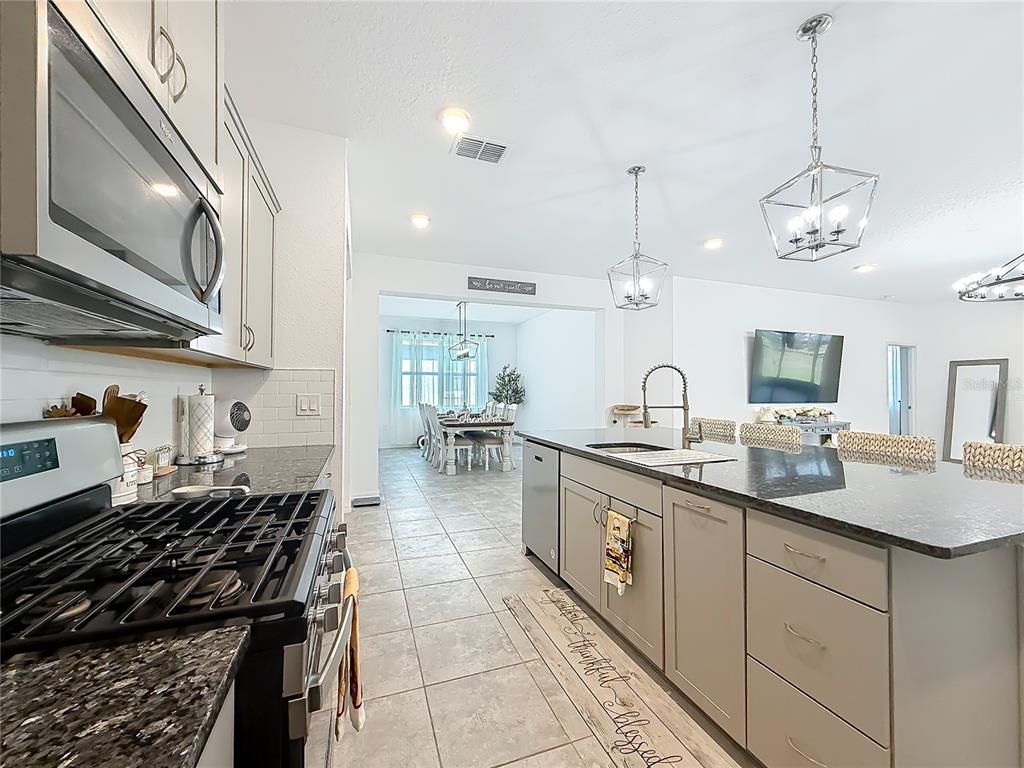 A modern kitchen features gray cabinets, granite countertops, stainless steel appliances, and a central island — 7429 SW 61ST STREET, OCALA, FL