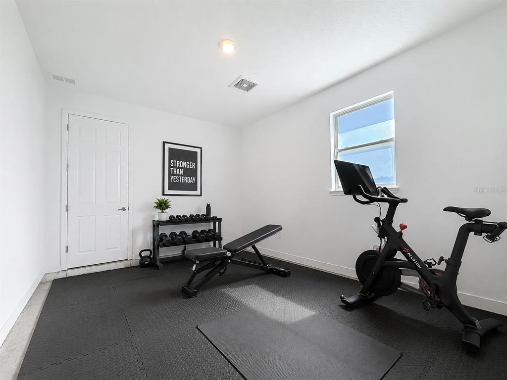 A home gym features a Peloton bike, a weight bench, dumbbells, and foam floor mats — 7429 SW 61ST STREET, OCALA, FL