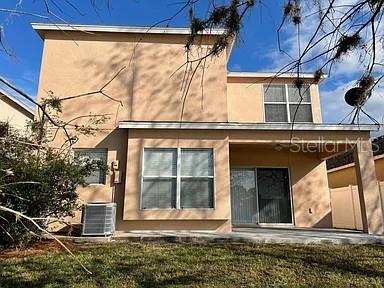 The rear exterior of a two-story tan stucco house features a covered patio and yard — 3449 HERON ISLAND DRIVE, NEW PORT RICHEY, FL