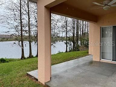 A covered concrete patio overlooks a grassy lawn and a lake lined with trees — 3449 HERON ISLAND DRIVE, NEW PORT RICHEY, FL