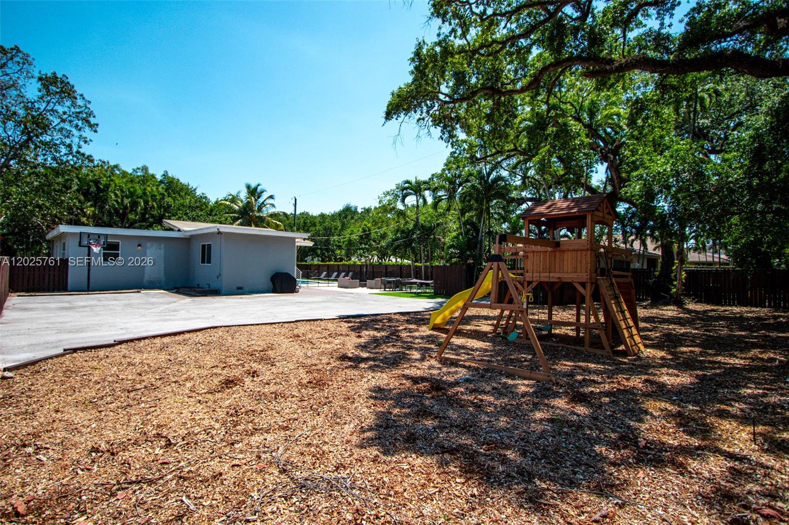 A backyard features a wooden playset, a concrete patio, and a gray house exterior — 3981 SW 58th St, Dania Beach FL 33312, DANIA BEACH, FL