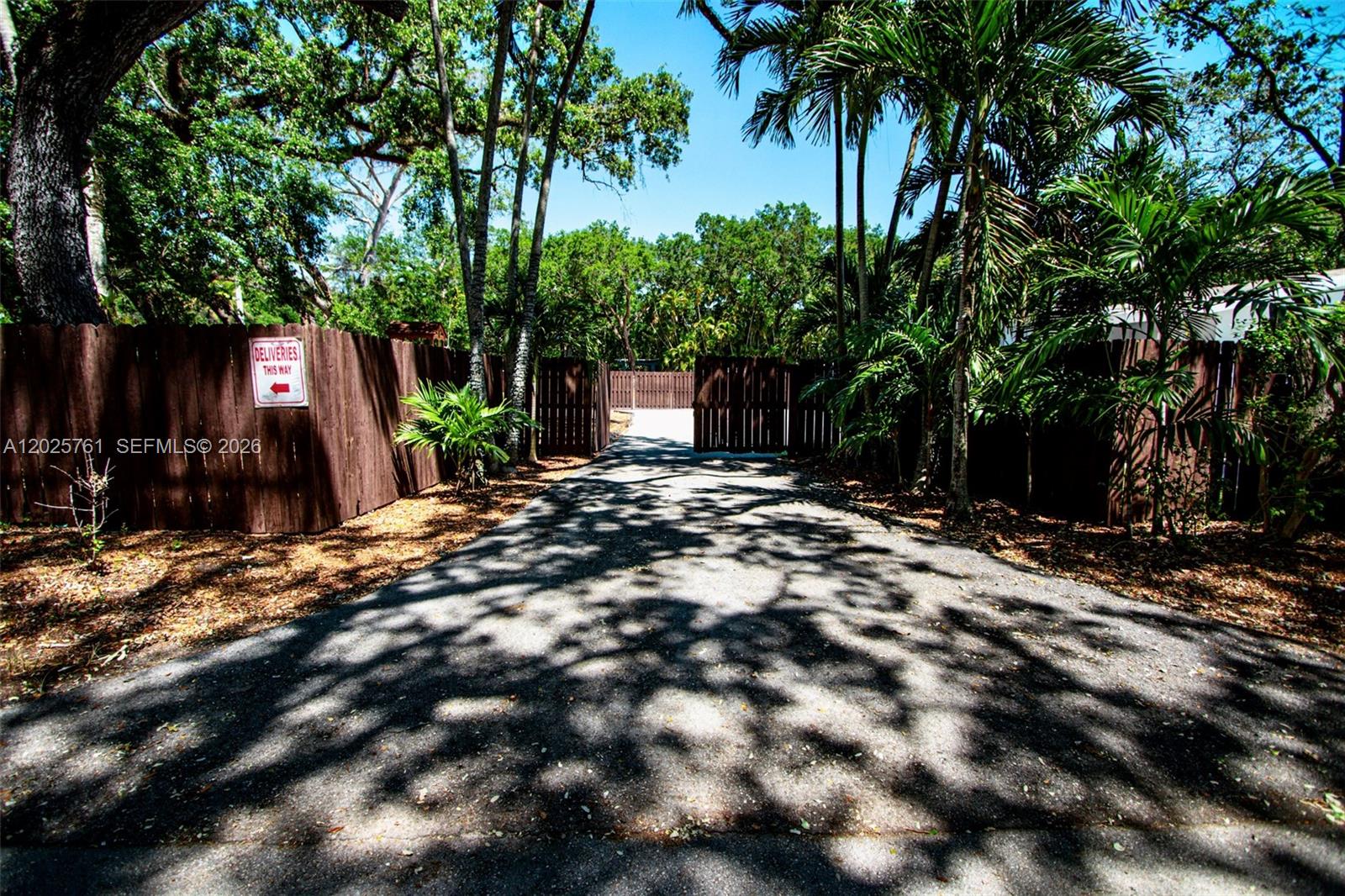 A paved driveway leads toward a wooden gate surrounded by trees and foliage — 3981 SW 58th St, Dania Beach FL 33312, DANIA BEACH, FL
