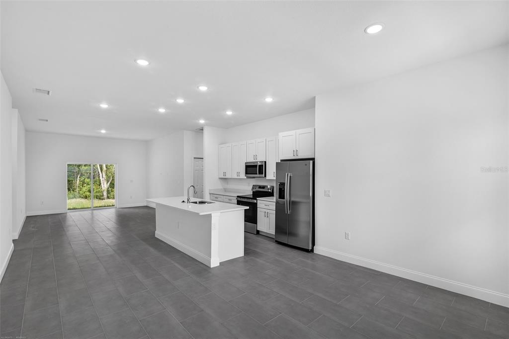 A modern kitchen with white cabinets, stainless steel appliances, and gray tile flooring — 22403 SW RAINBOW LAKES BOULEVARD, DUNNELLON, FL