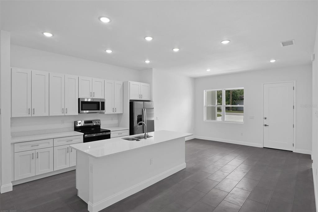 A modern kitchen features white cabinets, stainless steel appliances, a center island, and gray flooring — 22403 SW RAINBOW LAKES BOULEVARD, DUNNELLON, FL