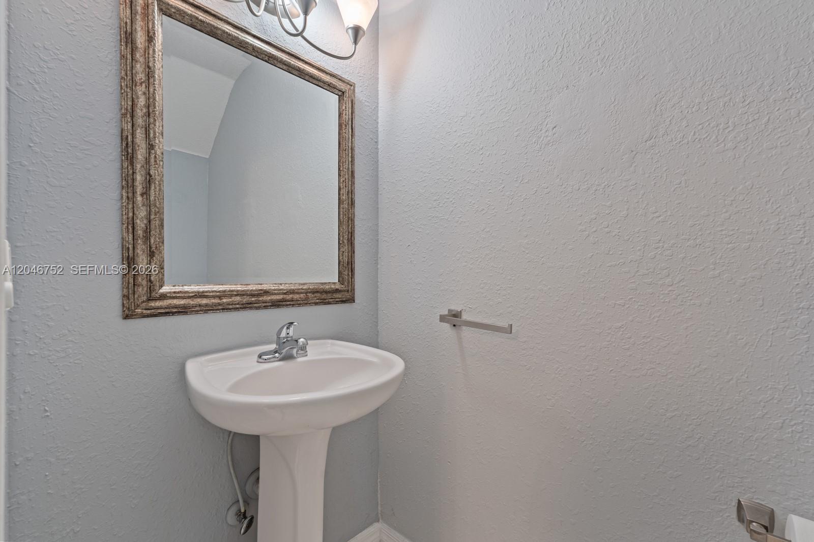 A pedestal sink and a framed mirror are mounted on a light blue wall — 3539 W 76th St # 6, Hialeah FL 33018, HIALEAH, FL