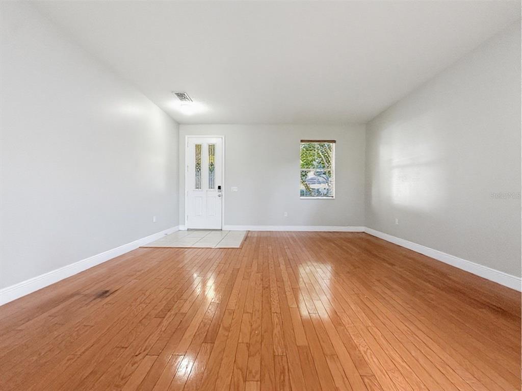 An empty room features light gray walls, hardwood flooring, and a white front door — 10250 MALPAS POINT, ORLANDO, FL