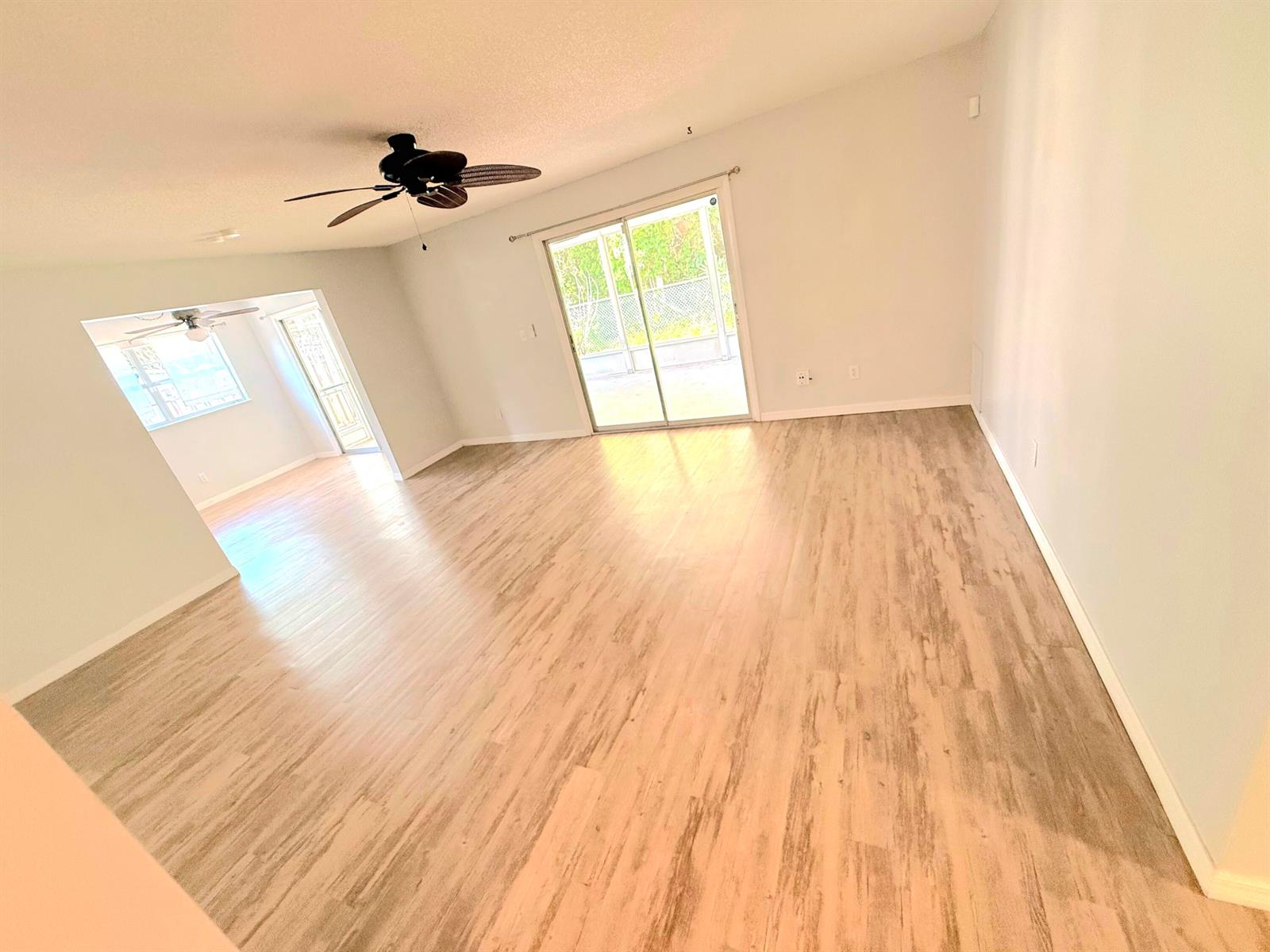 An empty living room with light wood-look flooring, a ceiling fan, and sliding glass doors — 2466 44th Avenue, Vero Beach FL 32966, VERO BEACH, FL