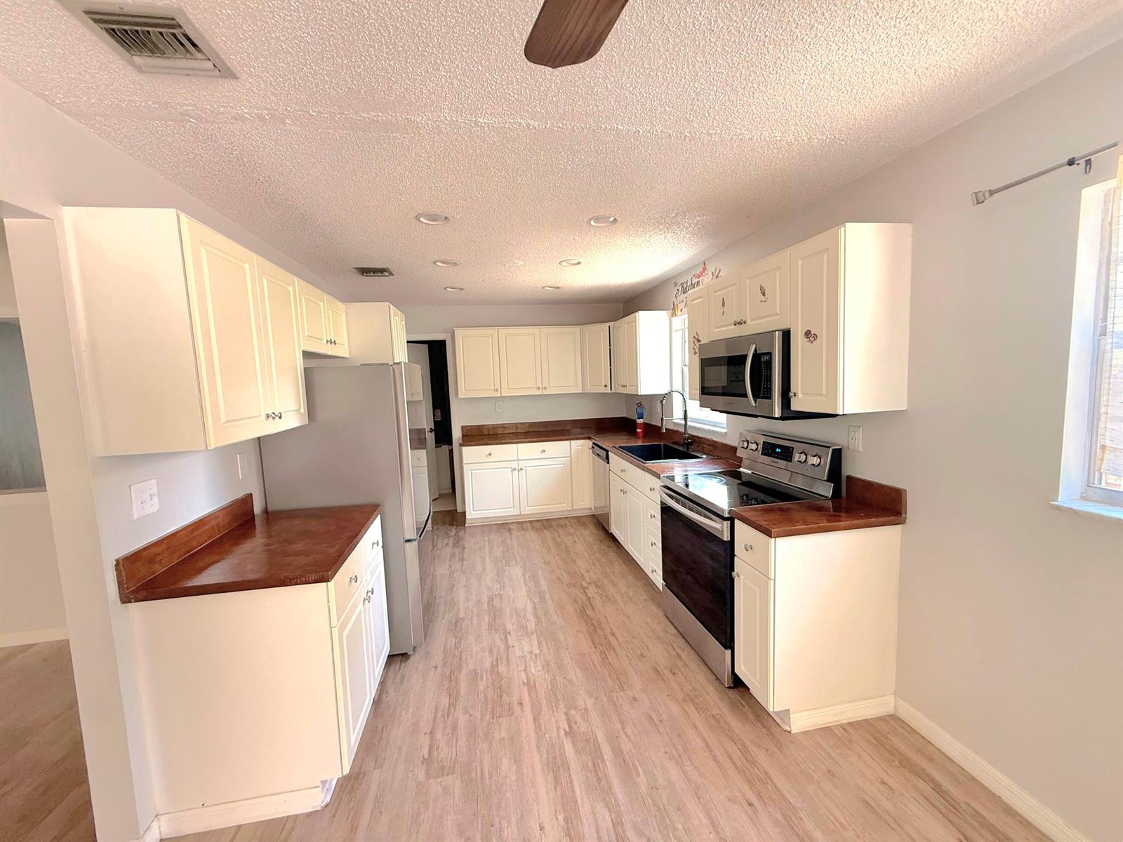 A kitchen features white cabinets, wood countertops, stainless steel appliances, and light wood-look flooring — 2466 44th Avenue, Vero Beach FL 32966, VERO BEACH, FL