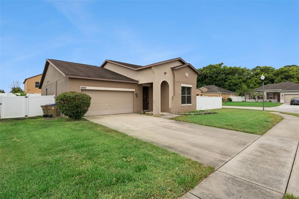 A tan single-story house with a two-car garage and a concrete driveway — 4882 ASHURST STREET, KISSIMMEE, FL