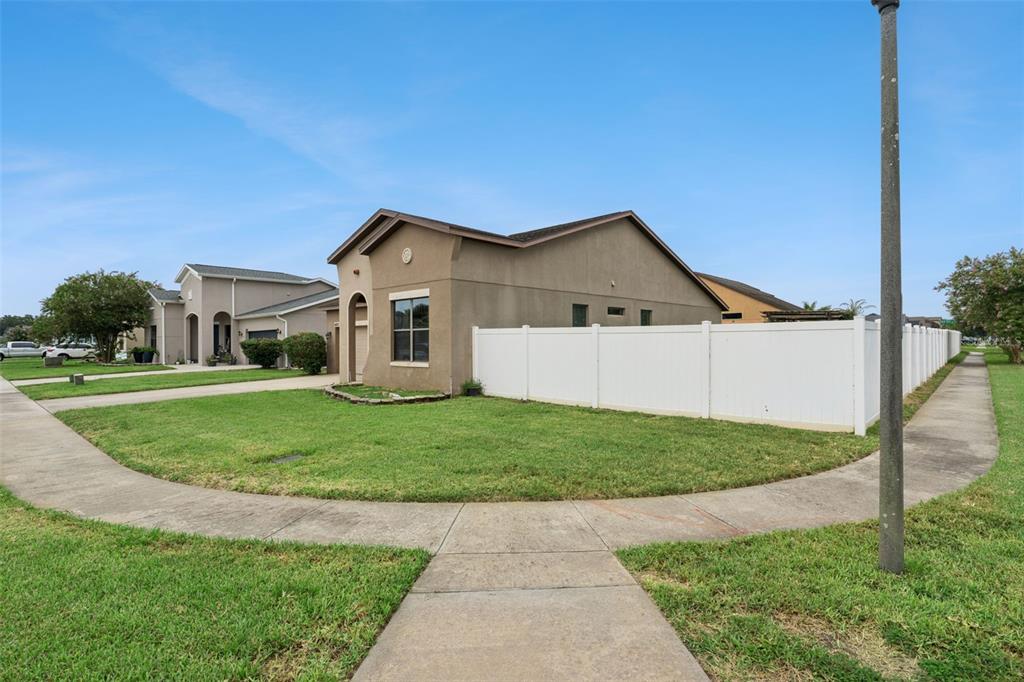 A tan single-story house with a white vinyl fence sits on a corner lot — 4882 ASHURST STREET, KISSIMMEE, FL