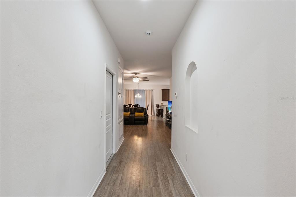 A hallway with light wood flooring leads into a living room with a ceiling fan — 4882 ASHURST STREET, KISSIMMEE, FL
