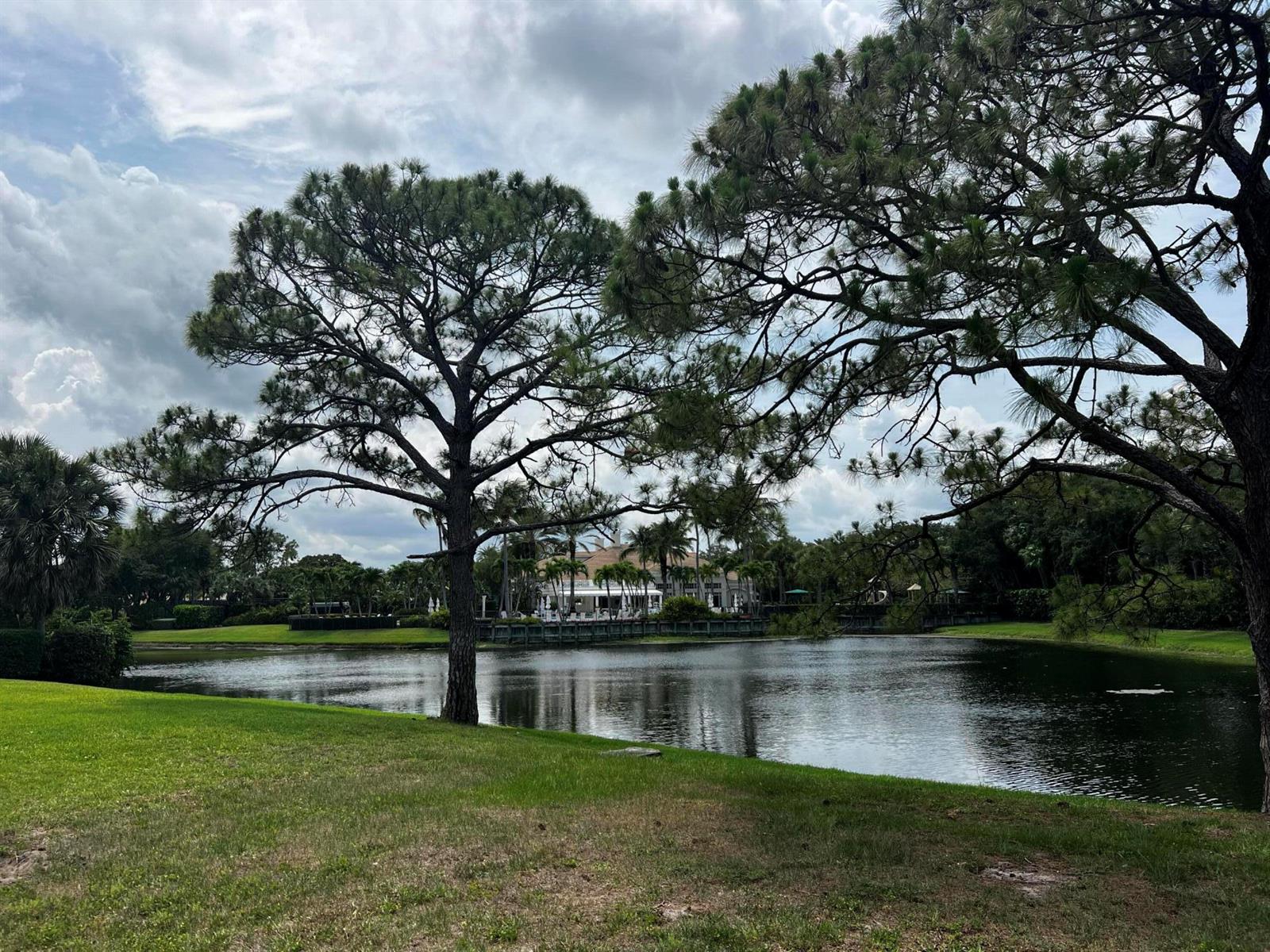 A pond sits in front of a building surrounded by trees under a cloudy sky — 111 Caballo Lane, Jupiter FL 33458, JUPITER, FL