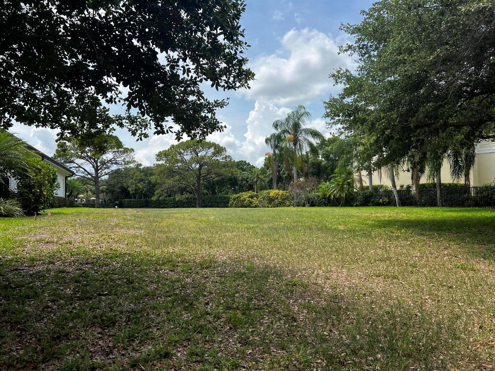 A large, grassy backyard features mature trees, palm trees, and a perimeter fence — 111 Caballo Lane, Jupiter FL 33458, JUPITER, FL