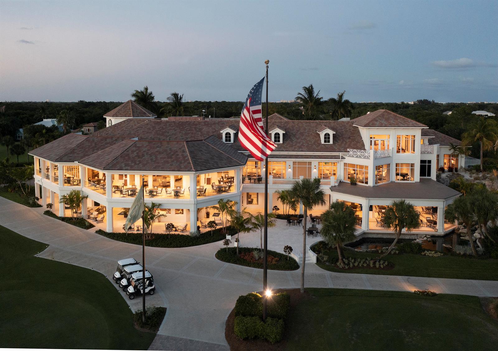 An aerial view of a large clubhouse exterior with a flag, golf carts, and landscaping — 111 Caballo Lane, Jupiter FL 33458, JUPITER, FL