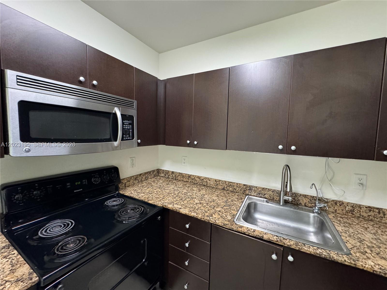 A kitchen features dark brown cabinets, granite countertops, a stainless steel sink, and black appliances — 529 NE 62nd St # 404, Miami FL 33138, MIAMI, FL