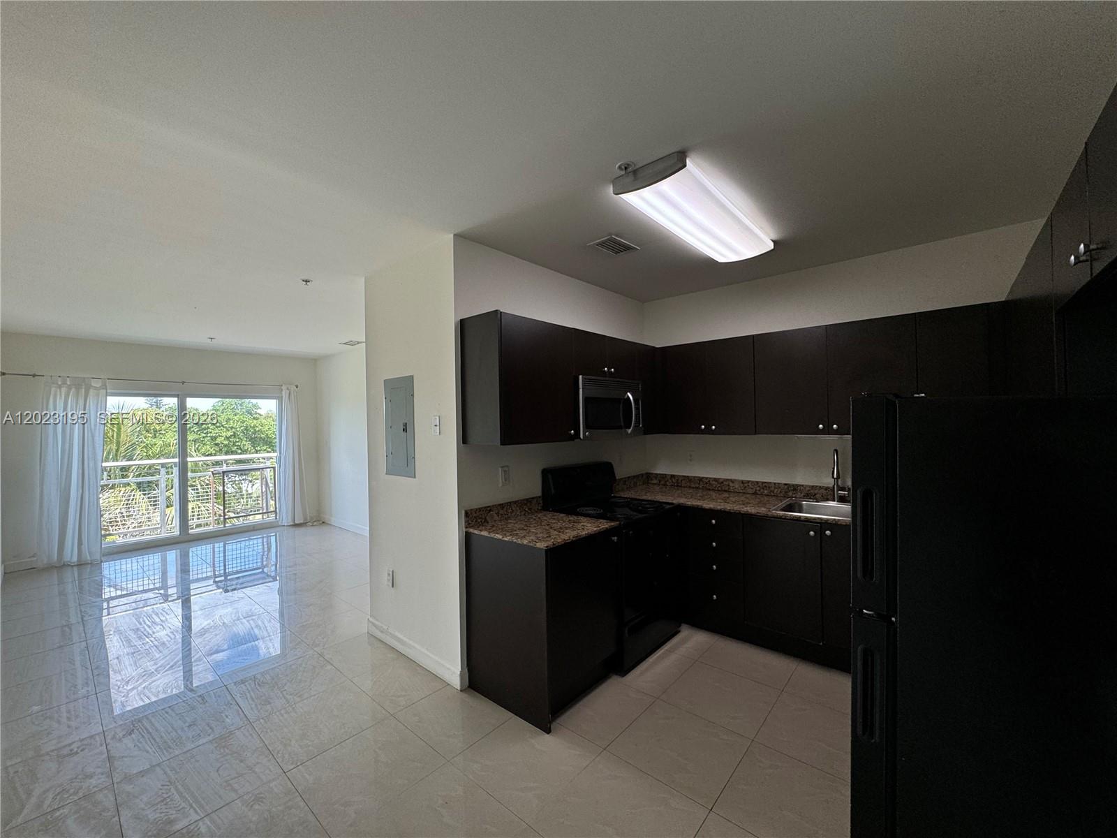 A kitchen with dark cabinets and granite countertops opens to a living area with balcony access — 529 NE 62nd St # 404, Miami FL 33138, MIAMI, FL