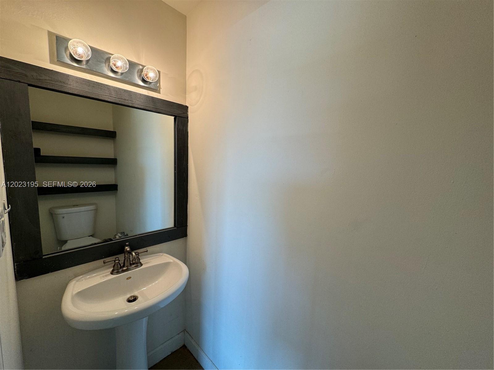 A bathroom features a pedestal sink, a dark-framed mirror, and wall-mounted shelves — 529 NE 62nd St # 404, Miami FL 33138, MIAMI, FL