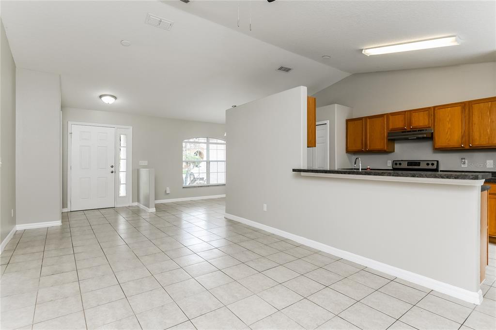 A tiled living area opens to a kitchen with wooden cabinets and a breakfast bar — 116 SAN BENITO WAY, KISSIMMEE, FL