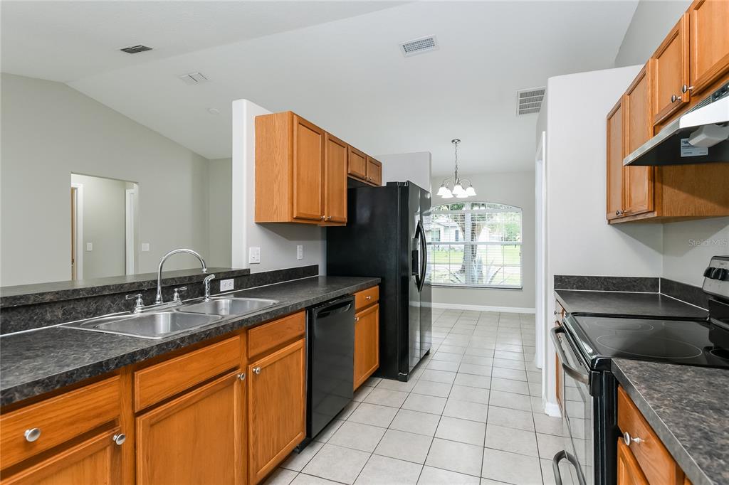 A kitchen features wood cabinets, dark laminate countertops, black appliances, and tile flooring — 116 SAN BENITO WAY, KISSIMMEE, FL