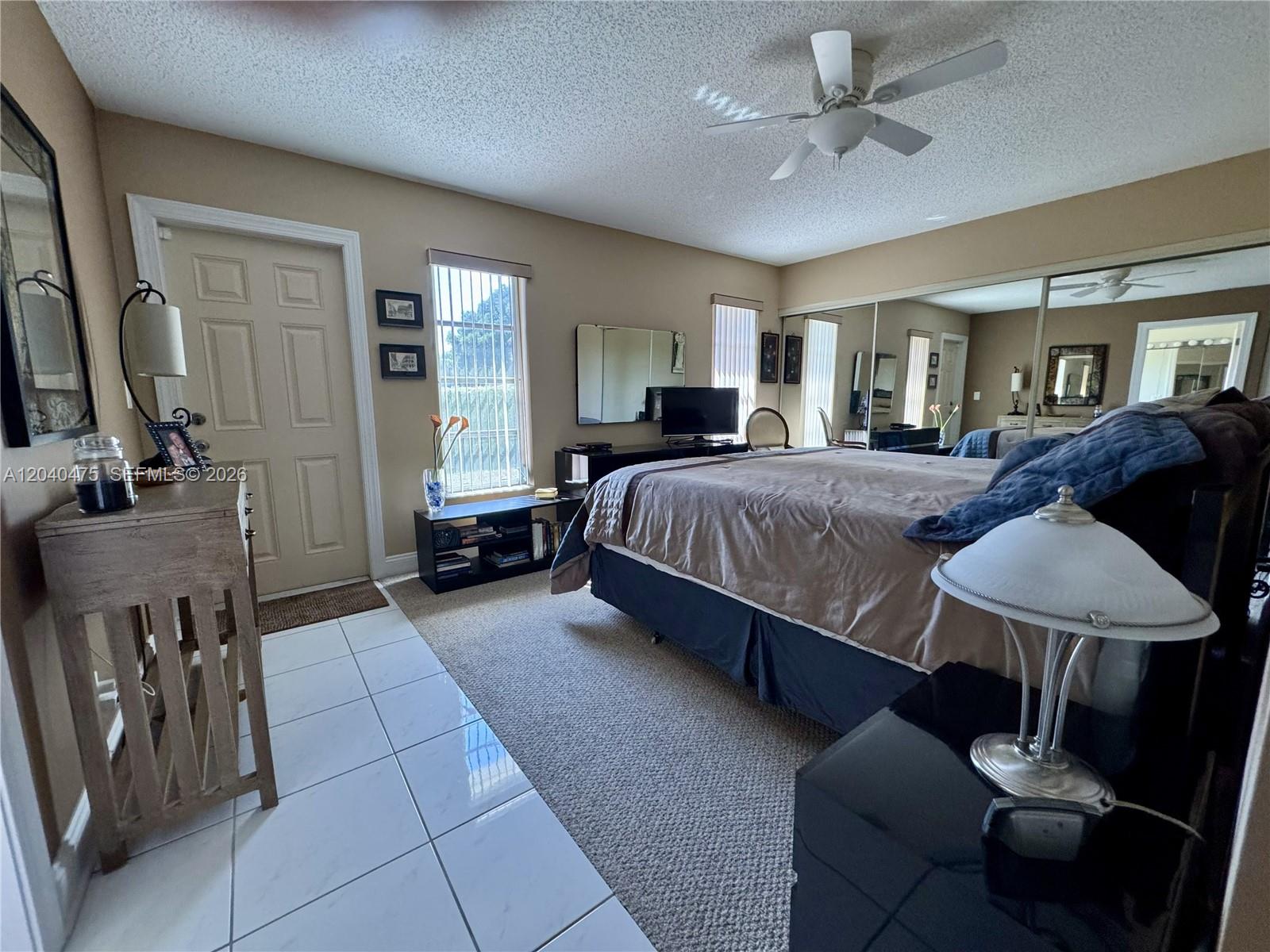 A bedroom features a bed, mirrored closet doors, tile and carpet flooring, and a ceiling fan — 5025 Lakefront Blvd # D, Delray Beach FL 33484, DELRAY BEACH, FL