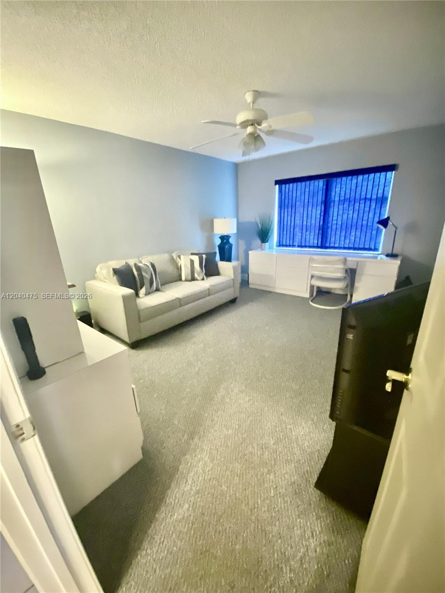 A living room features a light gray sofa, a desk with a chair, and carpeting — 5025 Lakefront Blvd # D, Delray Beach FL 33484, DELRAY BEACH, FL