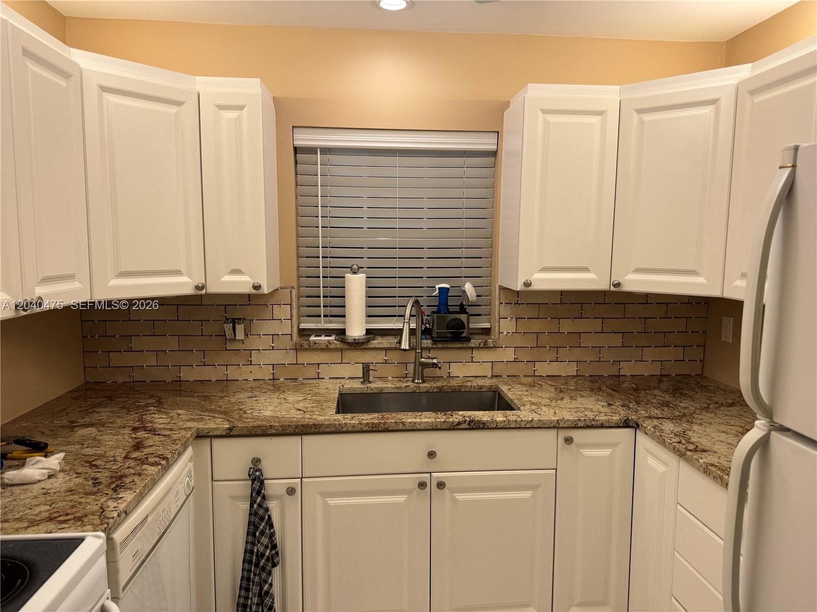 A kitchen features white cabinets, granite countertops, and an unfinished subway tile backsplash — 5025 Lakefront Blvd # D, Delray Beach FL 33484, DELRAY BEACH, FL