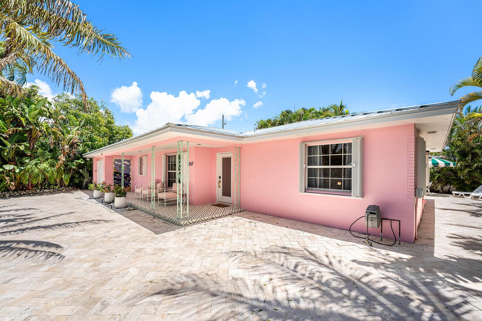 A pink single-story house features a tiled patio, metal roof, and decorative iron porch supports — 247 SE 3rd Avenue, Delray Beach FL 33483, DELRAY BEACH, FL