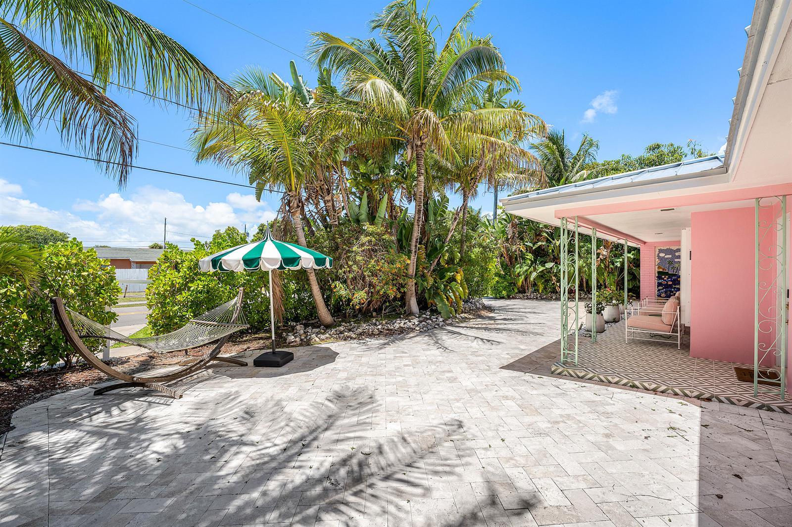 A patio with a hammock and umbrella sits beside a pink house with a porch — 247 SE 3rd Avenue, Delray Beach FL 33483, DELRAY BEACH, FL