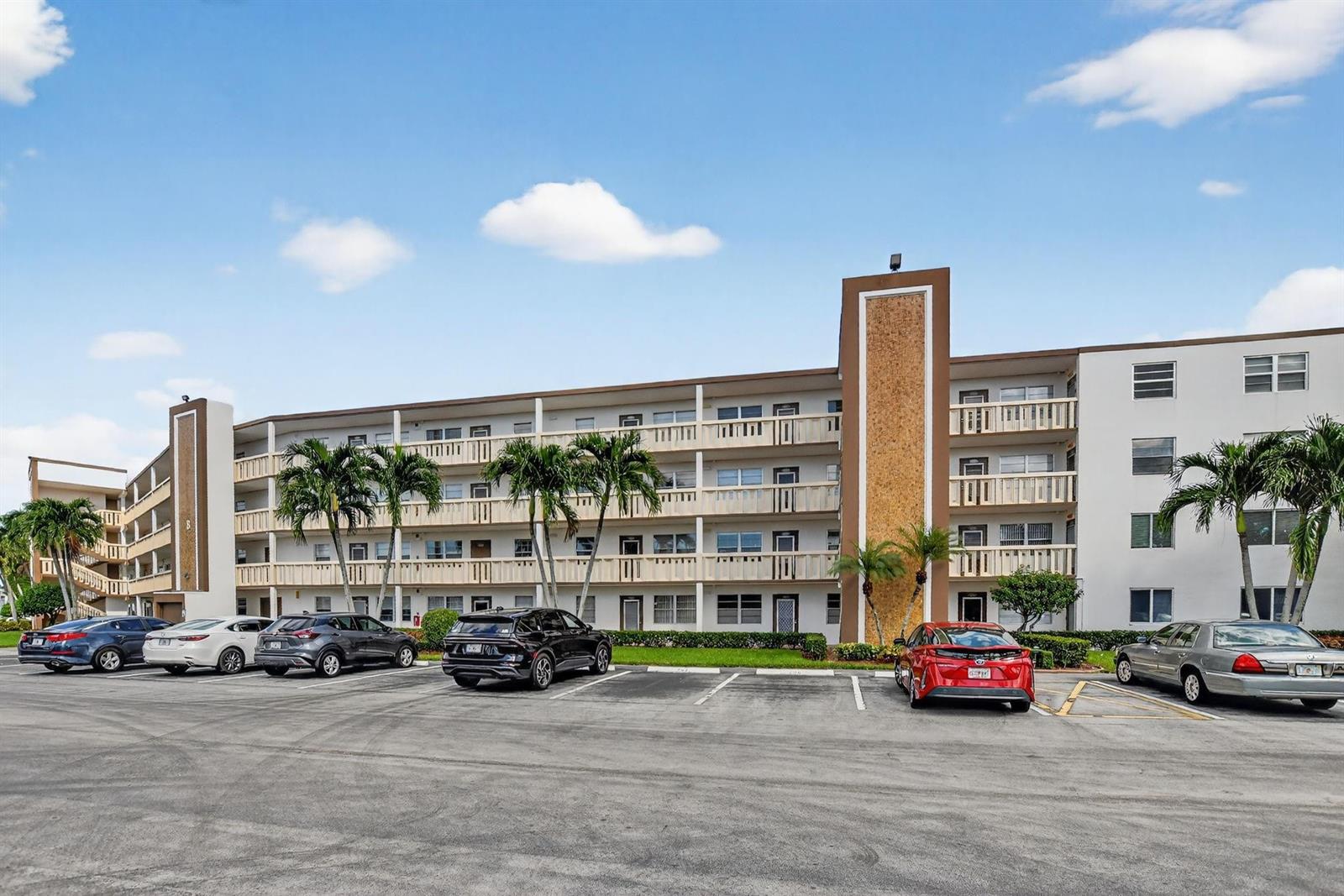A multi-story apartment building with a parking lot in the foreground under a blue sky — 3025 Guildford B # 3025, Boca Raton FL 33434, BOCA RATON, FL