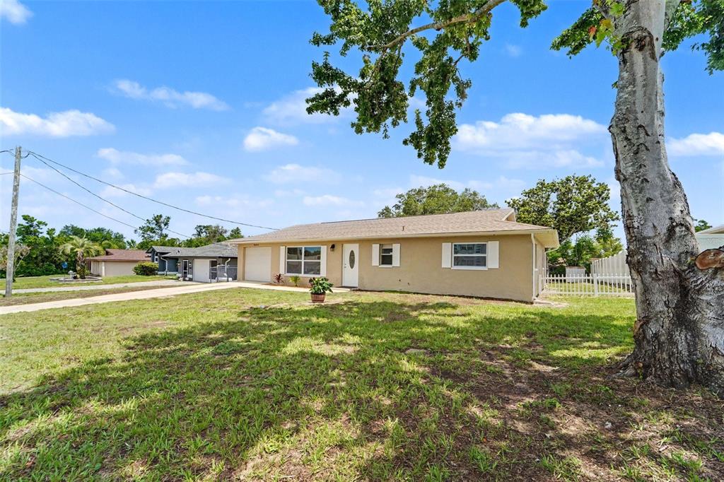 A single-story tan house with a white front door and a large tree in front — 9371 MALLARD STREET, SPRING HILL, FL