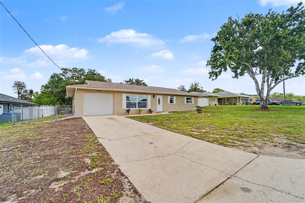 A single-story house with a beige exterior, a concrete driveway, and a large tree — 9371 MALLARD STREET, SPRING HILL, FL
