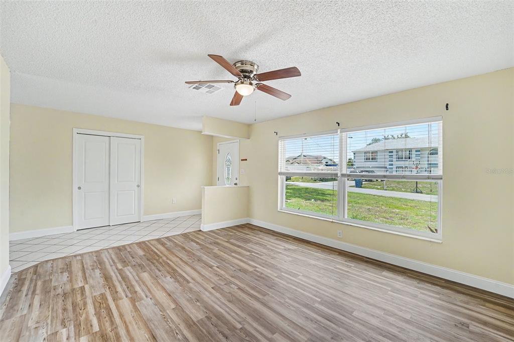 A living room features light yellow walls, wood-look flooring, a ceiling fan, and large windows — 9371 MALLARD STREET, SPRING HILL, FL