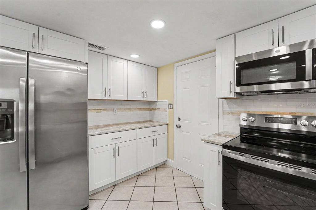 A kitchen features white cabinets, stainless steel appliances, a tiled backsplash, and light-colored countertops — 9371 MALLARD STREET, SPRING HILL, FL