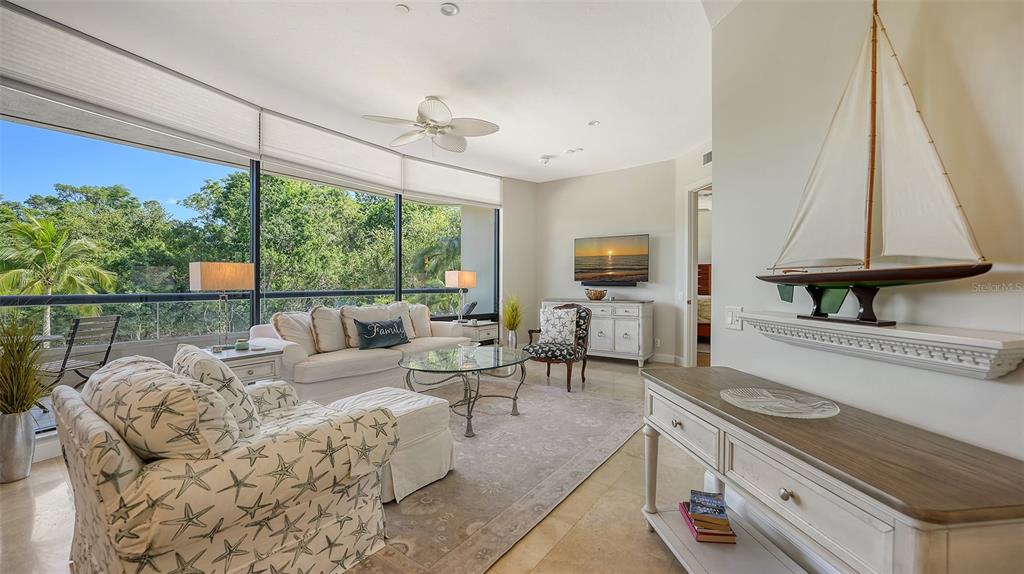 A living room features a large window, a sailboat model, and coastal-themed furniture — 1241 GULF OF MEXICO DRIVE UNIT 111, LONGBOAT KEY, FL