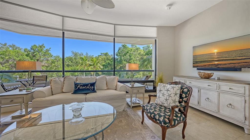 A living room features a sofa, patterned armchair, glass coffee table, and large floor-to-ceiling windows — 1241 GULF OF MEXICO DRIVE UNIT 111, LONGBOAT KEY, FL