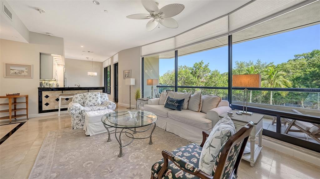 A living room features a white sofa, patterned armchairs, a glass coffee table, and large windows — 1241 GULF OF MEXICO DRIVE UNIT 111, LONGBOAT KEY, FL