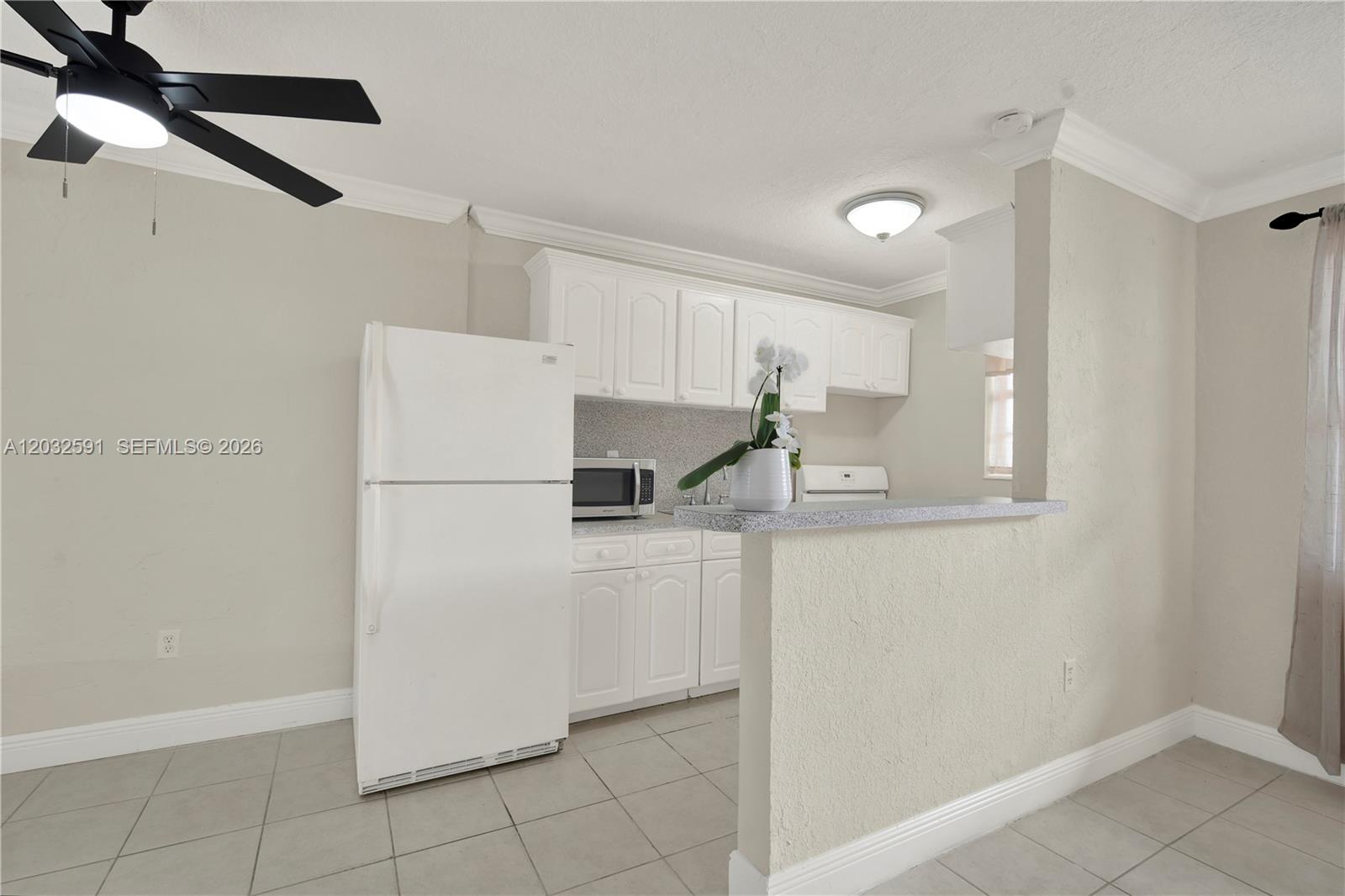 A kitchen features white cabinets, a white refrigerator, and a breakfast bar with tile flooring — 3855 SW 79th Ave # 45, Miami FL 33155, MIAMI, FL