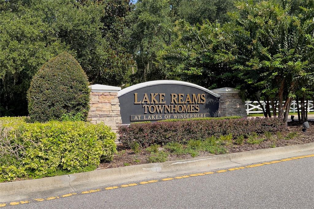 A stone and metal monument sign for Lake Reams Townhomes sits beside a paved road — 12744 LANGSTAFF DRIVE, WINDERMERE, FL