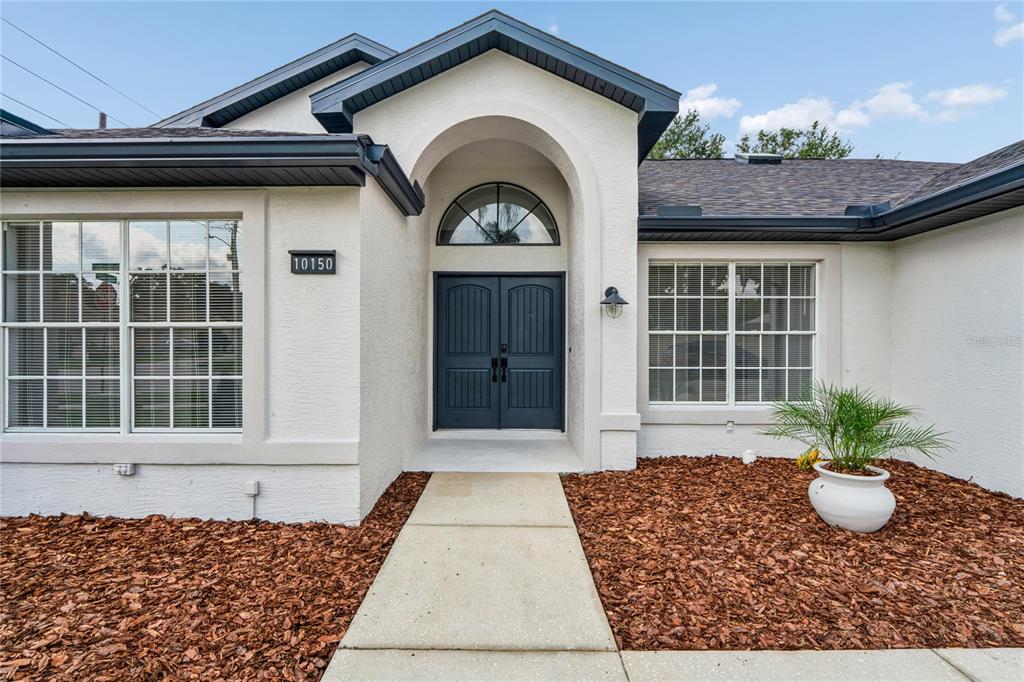 The exterior of a house features a white stucco facade, dark blue double doors, and mulch — 10150 HERMOSILLO, NEW PORT RICHEY, FL