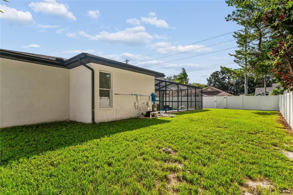 The exterior of a house features a grassy backyard, a pool enclosure, and white fencing — 10150 HERMOSILLO, NEW PORT RICHEY, FL