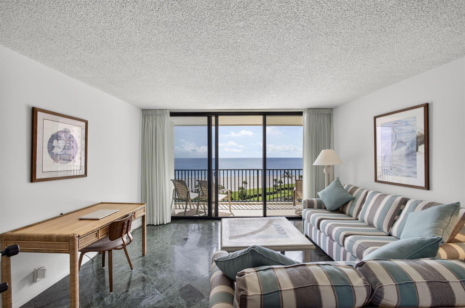 A living room with a striped sofa, desk, marble floors, and a balcony overlooking the ocean — 400 Ocean Trail Way # 807, Jupiter FL 33477, JUPITER, FL