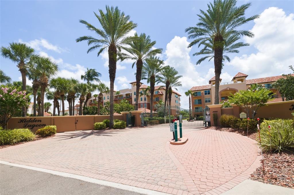 The gated entrance to the Hidden Lagoon community features a brick driveway and palm trees — 1645 PINELLAS BAYWAY S UNIT A1, TIERRA VERDE, FL