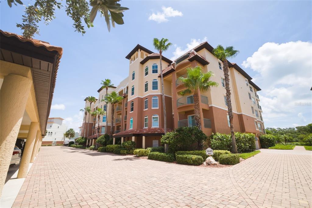A multi-story apartment building with a paved driveway and palm trees under a blue sky — 1645 PINELLAS BAYWAY S UNIT A1, TIERRA VERDE, FL