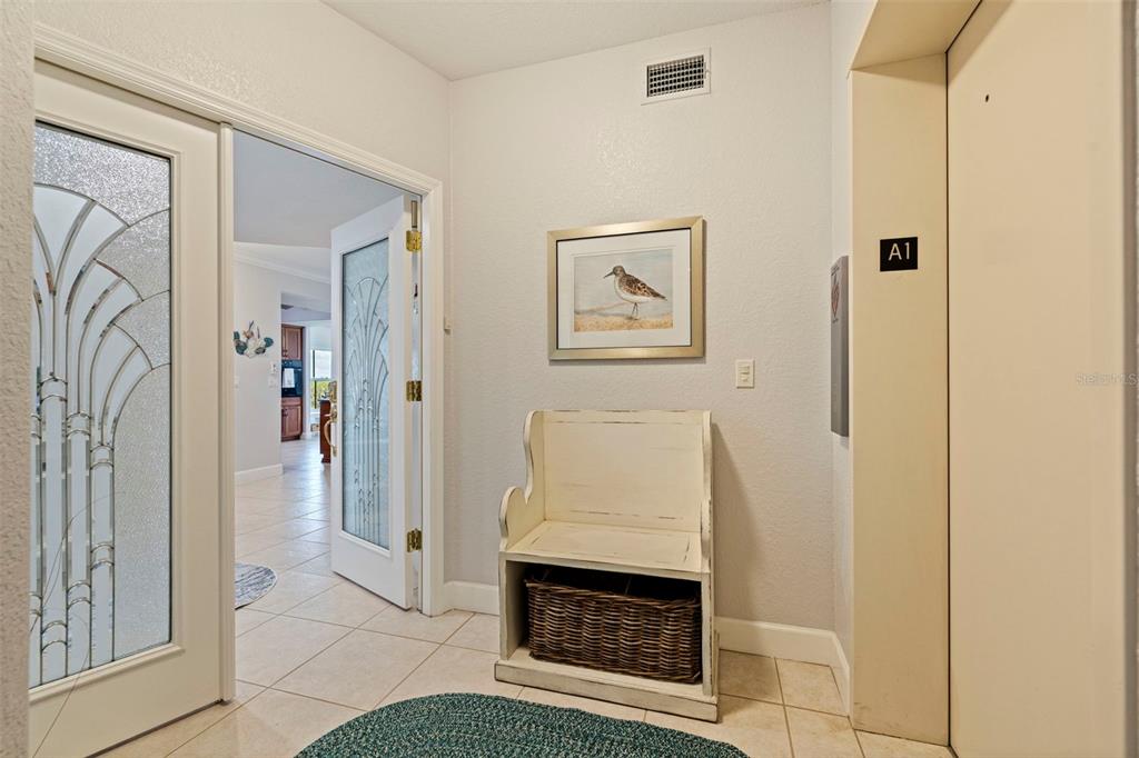 An entryway features a white wooden bench, a framed bird print, and an elevator door — 1645 PINELLAS BAYWAY S UNIT A1, TIERRA VERDE, FL