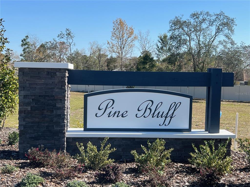 A stone and dark wood monument sign displays the name Pine Bluff in a neighborhood — 4962 SUTHERLAND STREET Lot 72, SPRING HILL, FL