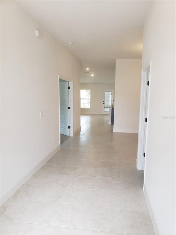 A hallway with light-colored tile flooring leads toward an open-concept living area and kitchen — 4962 SUTHERLAND STREET Lot 72, SPRING HILL, FL