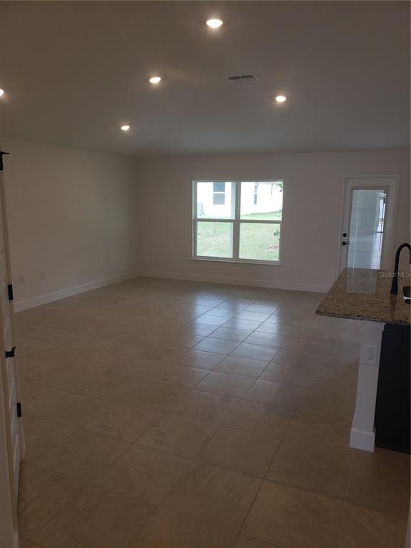 An open-concept living area features light-colored tile flooring, recessed lighting, and a granite-topped kitchen island — 4962 SUTHERLAND STREET Lot 72, SPRING HILL, FL