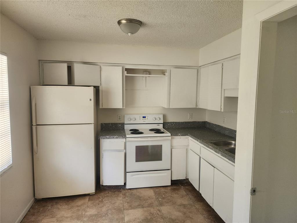 A kitchen with white cabinets, white appliances, speckled countertops, and tiled flooring — 10020 N HYACINTH AVENUE, TAMPA, FL