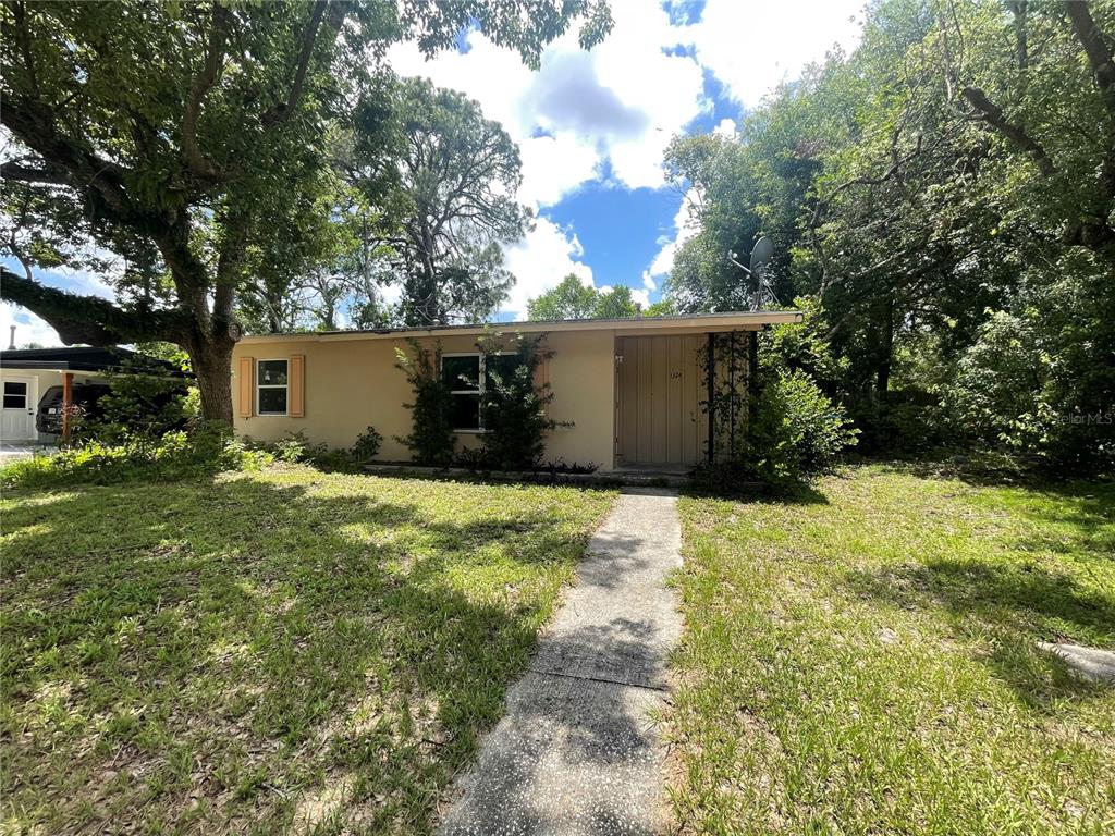 A single-story house with a beige exterior, a concrete walkway, and surrounding trees — 1324 WHITEWOOD DRIVE, DELTONA, FL