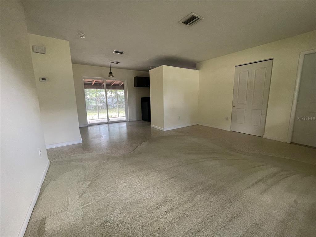 A living room with beige carpeting, a sliding glass door, and a white interior door — 1324 WHITEWOOD DRIVE, DELTONA, FL